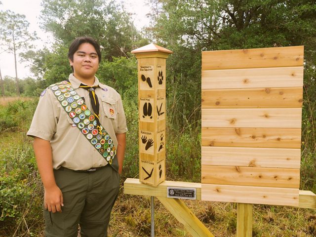 Eagle Scout standing beside a wooden public exhibit at Tiger Creek Preserve.