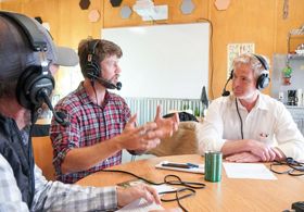 Three men sitting at a table with headphones mics on