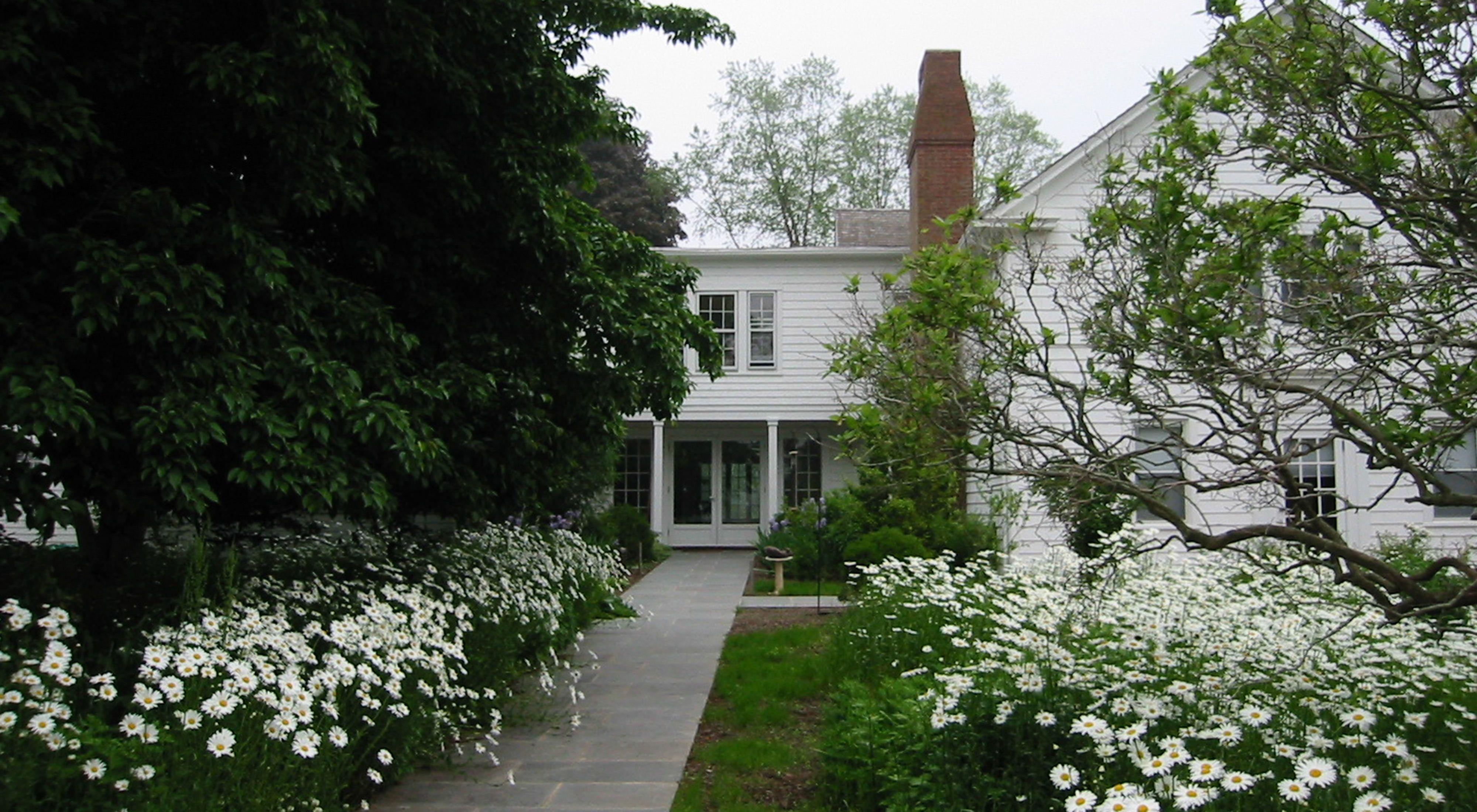 White building behind gardens of white flowers and trees.