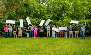 A group of people standing in green grass celebrate while holding large checks in the air. 
