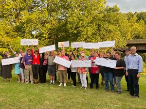 A group of people pose together, many of them holding up large novelty checks, during an event celebrating grant recipients.
