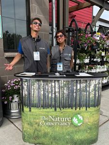 Two of our F2F canvassers smiling behind a TNC banner beside a flower stand.