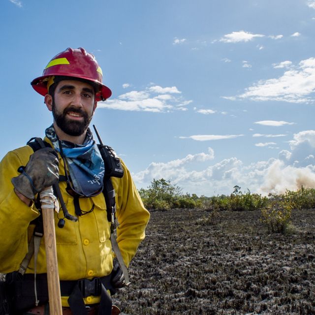 Portrait of Chase McLean holding the handle of a shovel, standing in front of a freshly burned pasture, taken during a wildfire supression training.