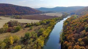  Aerial view of a river in New York with autumn-colored hillsides in the background.