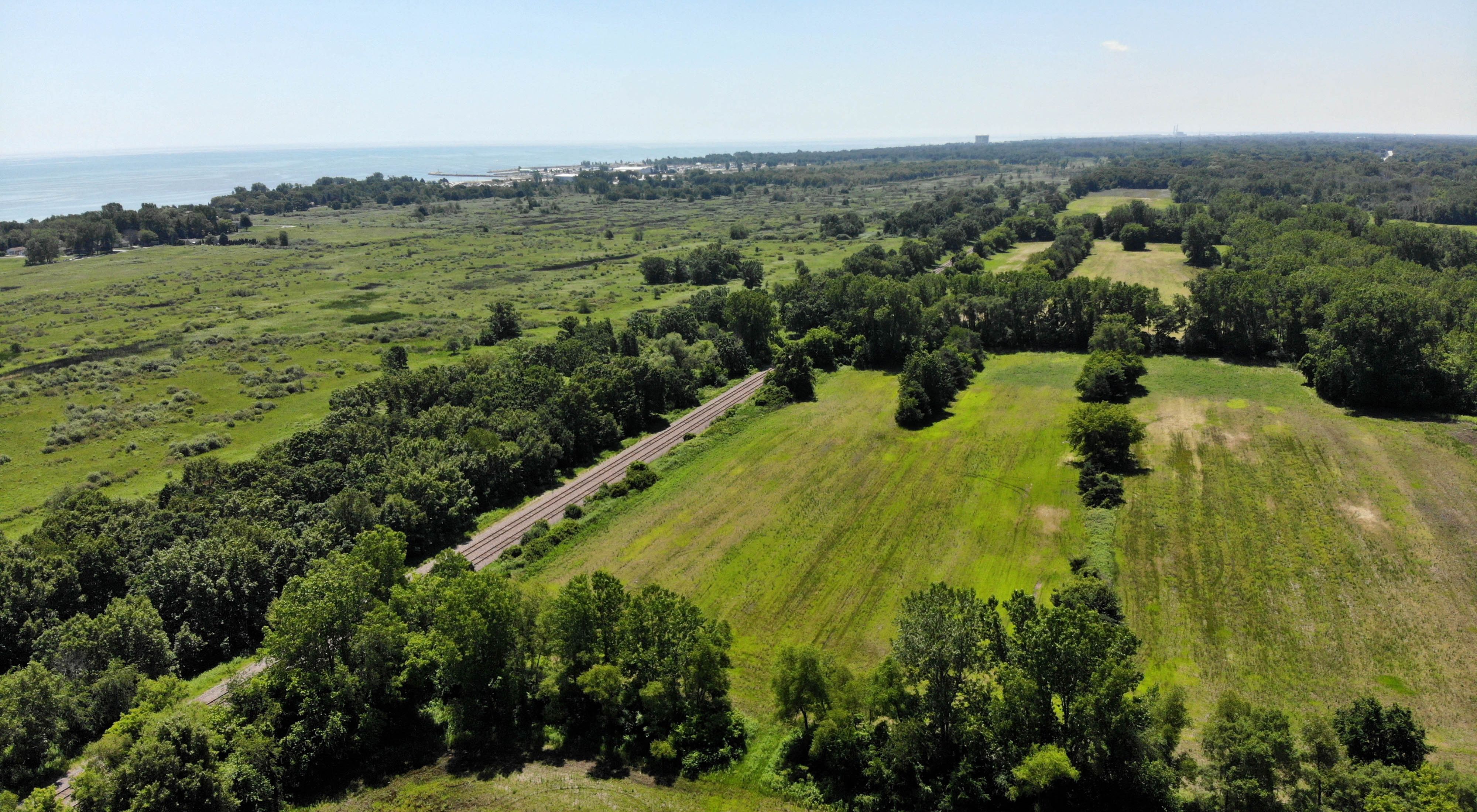 Aerial photo showing the restoration area in the foreground with open land and trees, the Chiwaukee Prairie wetlands beyond that and Lake Michigan in the distance.