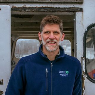 A man in a blue fleece stands on a fishing boat smiling.