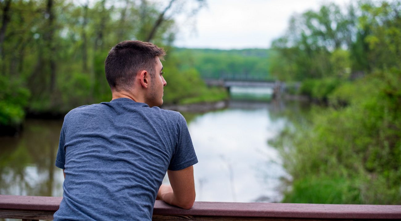 A person leaning on a railing and looking out over a river.