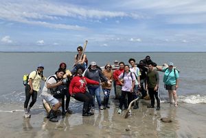 A group of students post with TNC staff on Parramore Island, standing at the edge of the beach in ankle deep surf.