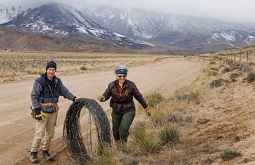 Two people roll up barbed-wire fencing.