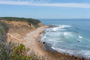Tall bluffs on the left rise high above a rocky beach with the light blue ocean stretching to the horizon. 