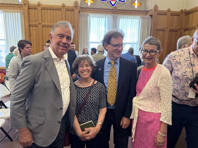 Four people wearing business attire pose for a photo at an event.