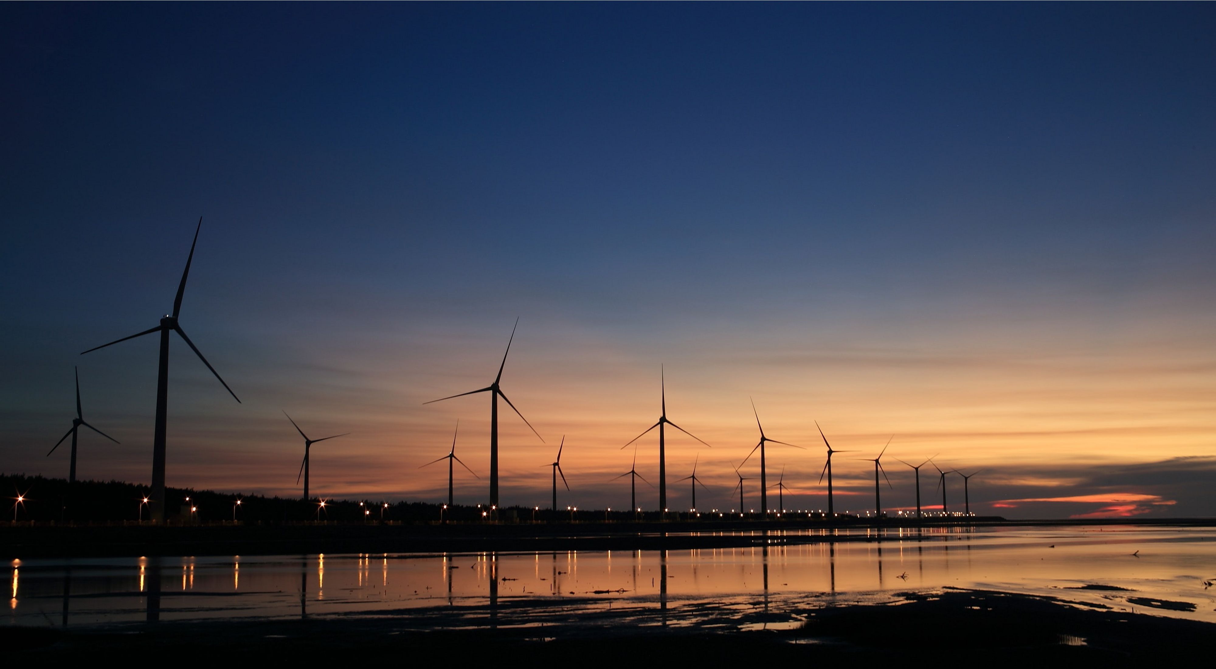 Wind turbines dot a shoreline at sunset.