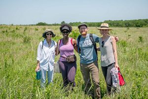 A group of four people stand amongst bright green prairie grass at Clymer Meadow. 
