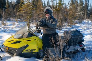 A smiling person wearing a helmet sits on a snowmobile.