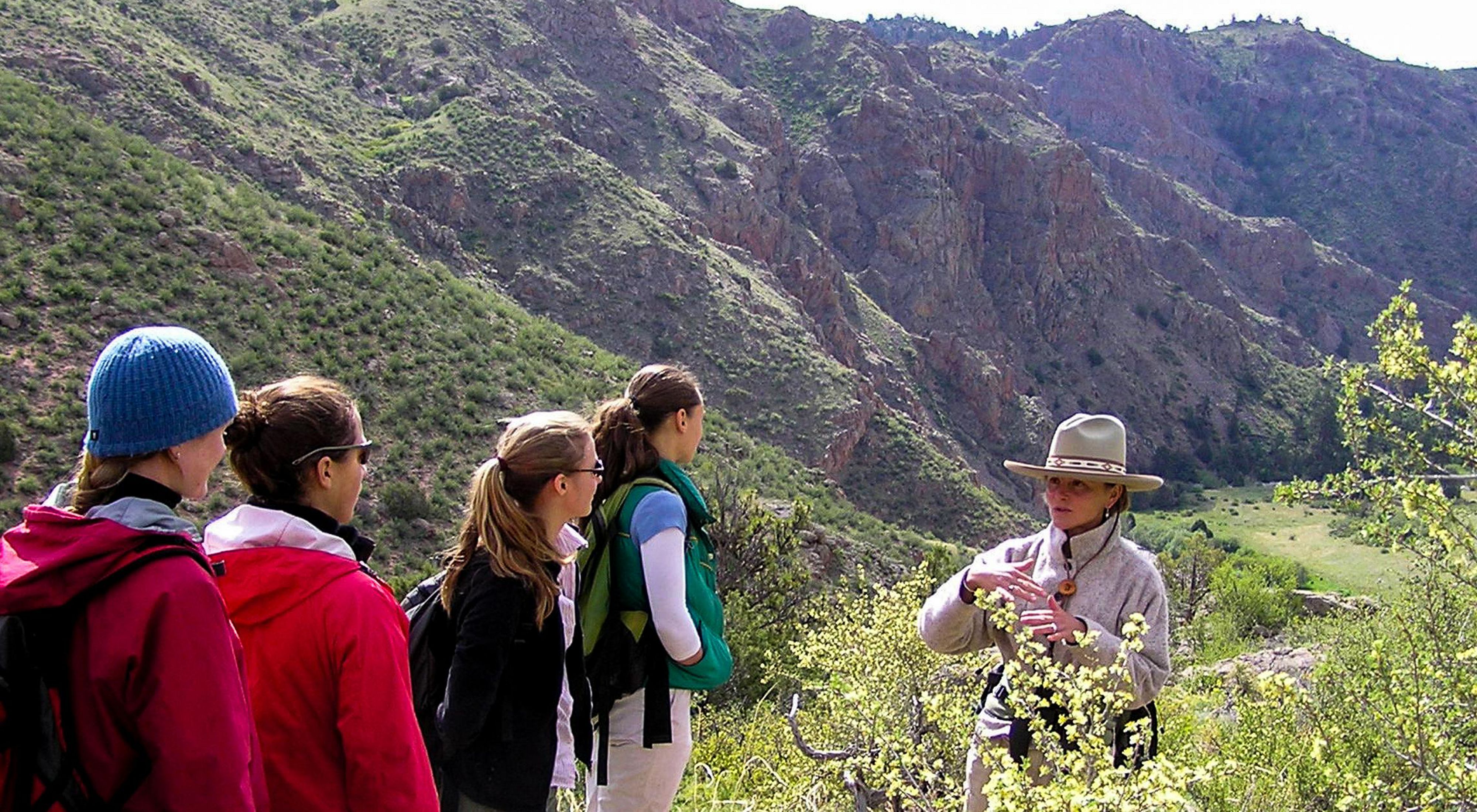 A hiking guide is talking to four hikers in a canyon.