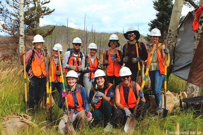 Two women standing in a field against trees.