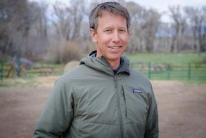 A man in a green raincoat smiling for a headshot.