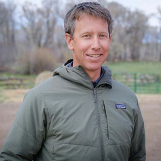 A man in a green raincoat smiling for a headshot.