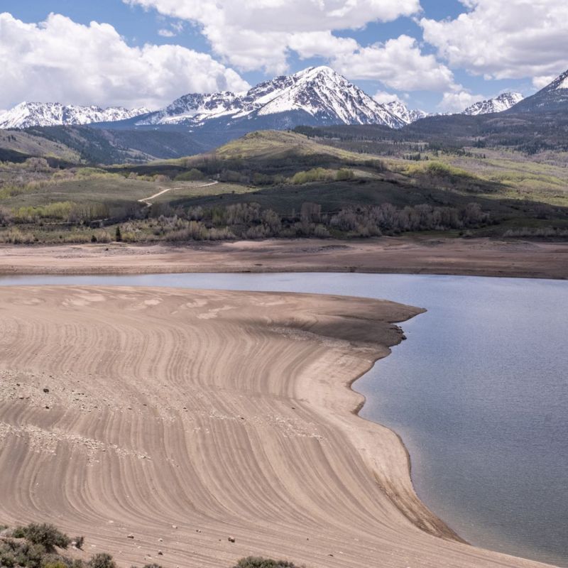 An aerial photo of a lake with snow capped mountains in the background.