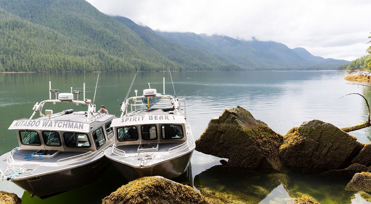 Two boats in a costal inlet surrounded by tree-covered hills.