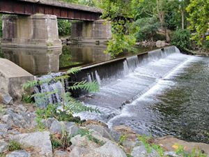 Waters flow over the Collins Lower Dam surrounded by cement structure.