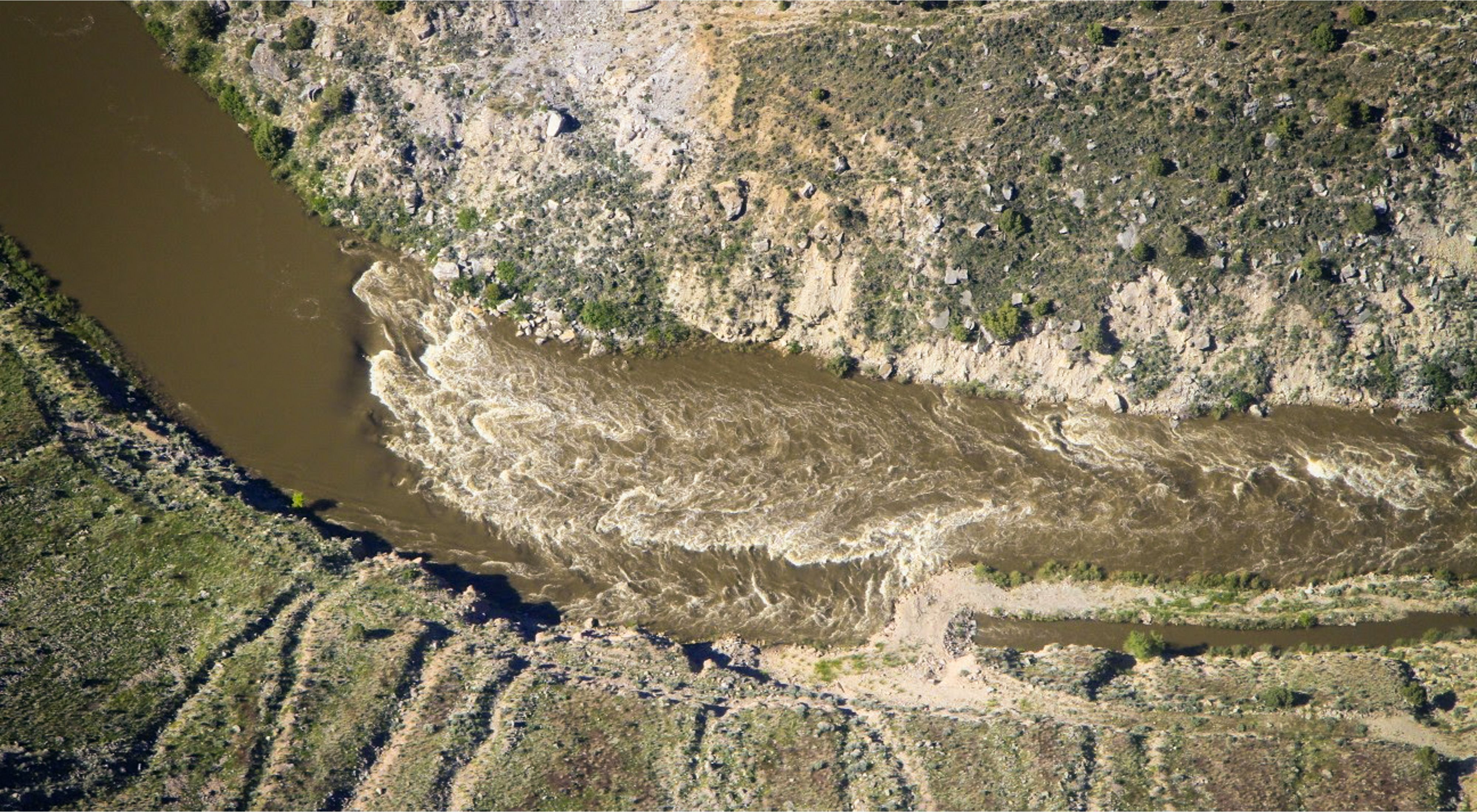 An aerial shot of a river flowing between grass hills.