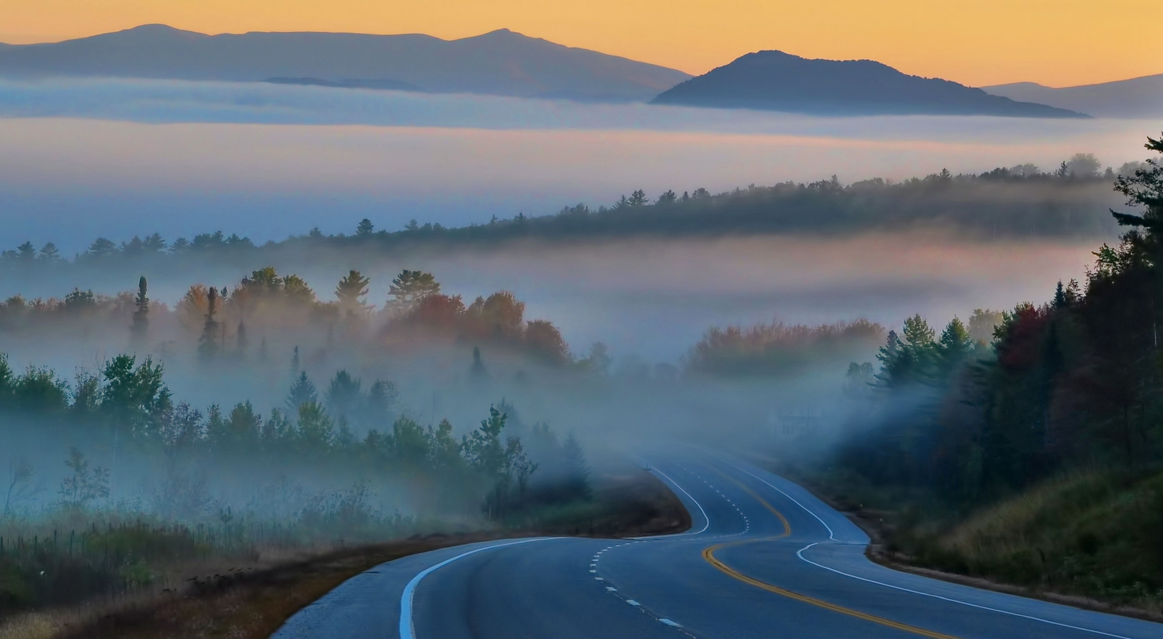 A highway winds through foggy, forested mountains.