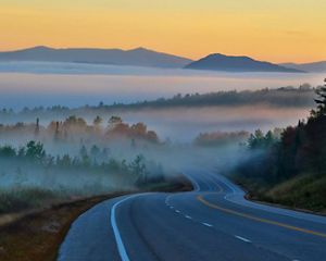 A highway winding through foggy, forested mountains.
