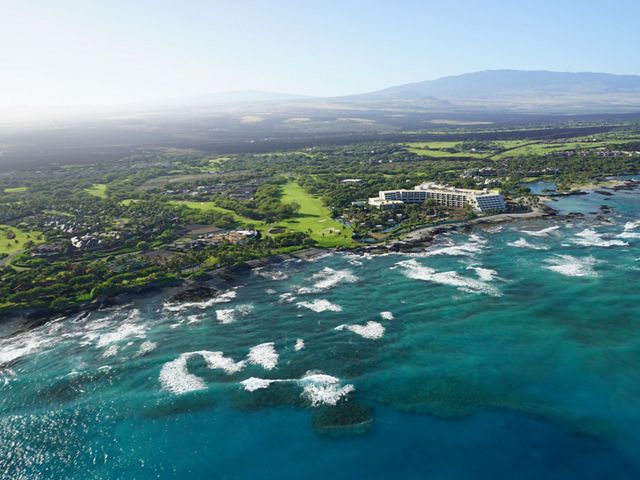 Aerial view of a coastline in Hawaii, with waves breaking along coral reefs before reaching the shore.