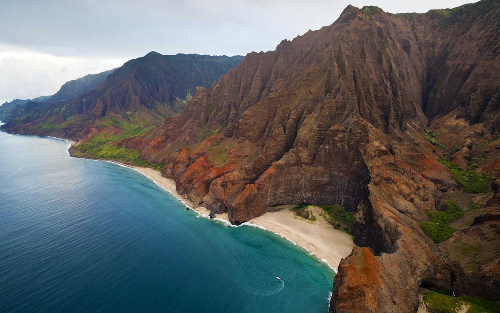 Aerial view of a tour boat near the high cliffs of the Na Pali Coast in Hawaii. 