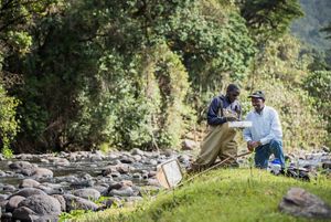 Two men sitting alongside a riverbank engage in river monitoring.
