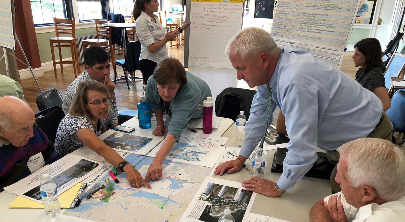 A group of people gather around a table to look at maps.