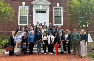 A group of people stand in rows on steps in front of a brick building.