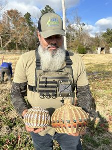 A man holds two homemade baskets in his hands.