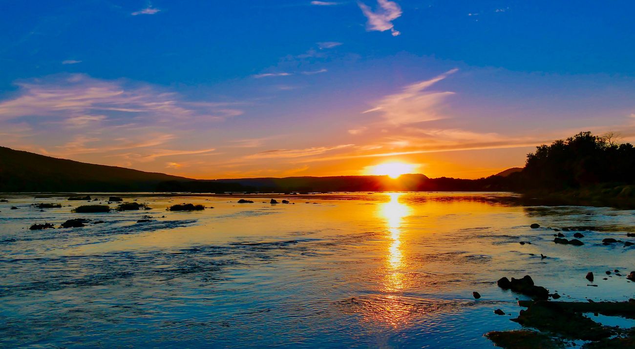 A sun sets over a body of water creating an orange reflection.