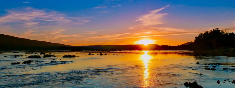 A sun sets over a body of water, creating a yellow and orange reflection.