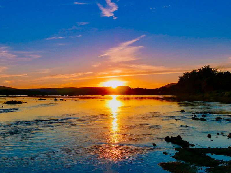 The sunsets over a body of eater creating a deep blue, purple, and pink sky.