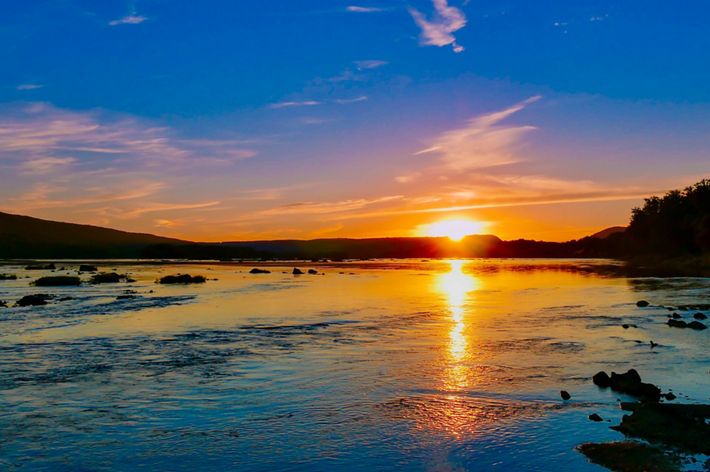 A sunsets over a body of water creating an orange reflection.