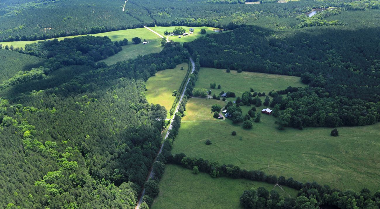 An aerial image of a farm with green fields, verdant forests and a red barn.
