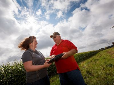 Crop advisor and farmer standing next to farm field.