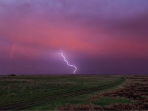 Lightning strikes the prairie from a pink-purple colored sky.