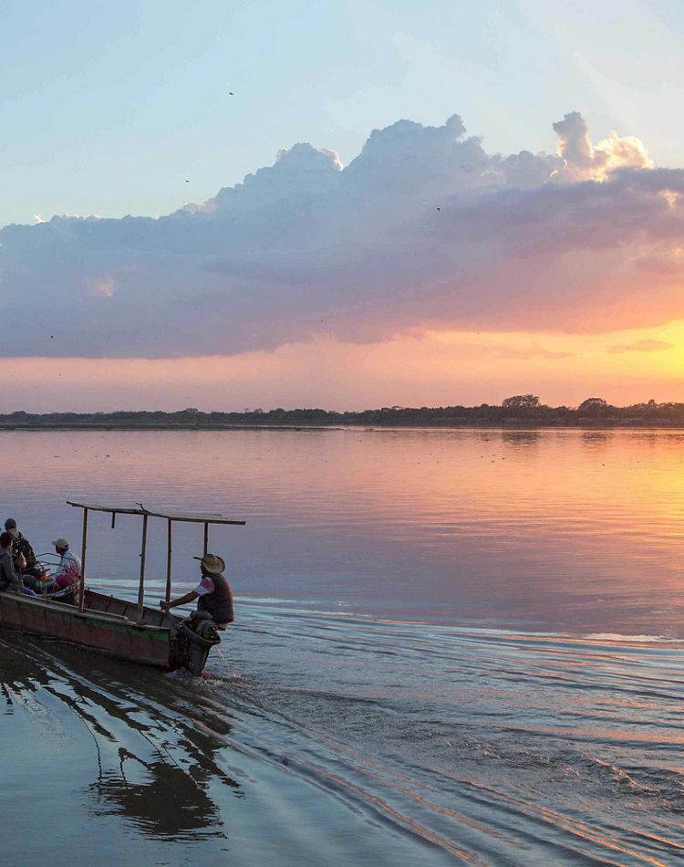 boat ferries people across river with ripples at sunset