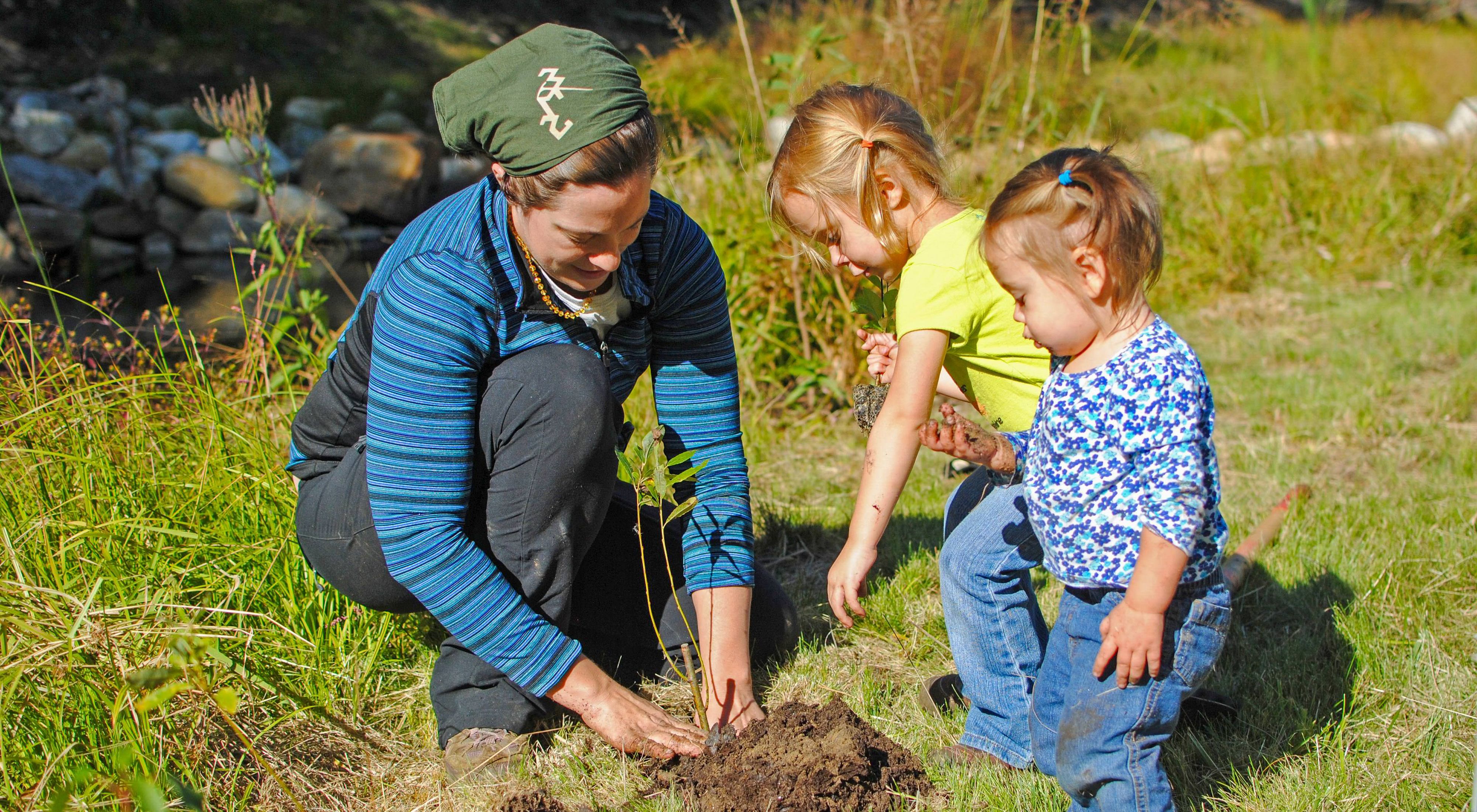 A volunteer plants a tree with help from two young children.