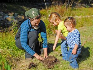 A volunteer and two small children plant a tree.