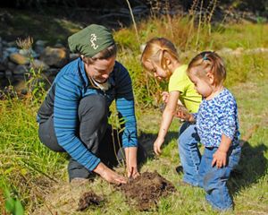 A volunteer and two small children plant a tree.