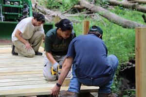 Three people repair a boardwalk trail.