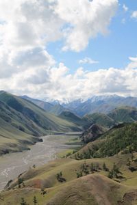 Aerial view of the Mongolian Mountains with lush green valleys and meandering rivers under a partly cloudy sky.