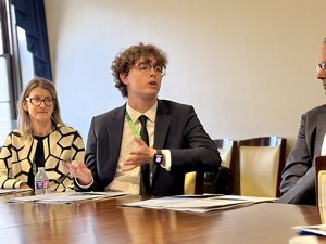 A person gestures during a discussion at a conference table with two other attendees looking on, in a well-lit meeting room.