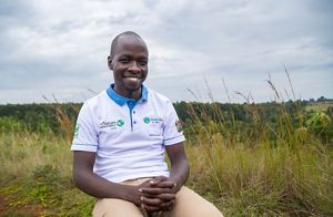 A woman stands in front of a lake with mountains in the background. 