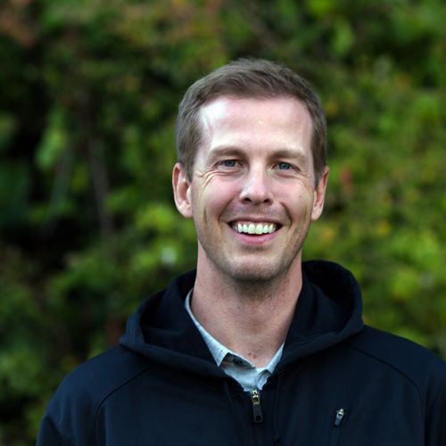 an outdoor headshot of a dark-haired man